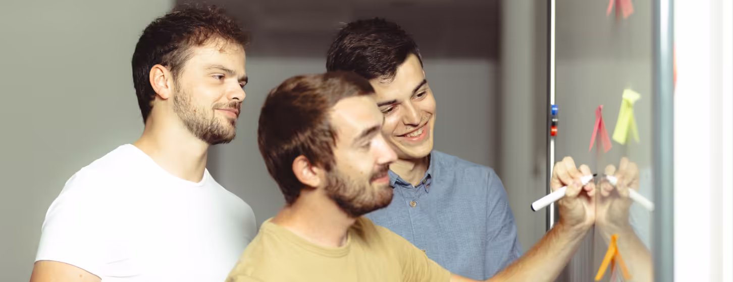trois personnes écrivant sur un tableau blanc